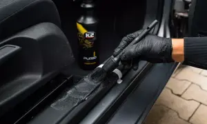 Szczotka z rękawiczką czyści plastikowe elementy progów, przygotowując je do detailing wnętrza. Obok butelka z preparatem K2 Purio.