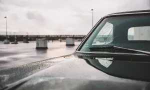 Krople deszczu spływają po szybie i masce samochodu, świadcząc o skutecznej powłoce hydrofobowej.