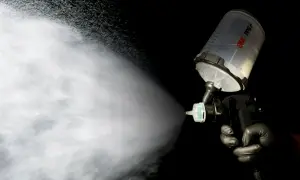 Ręka w czarnej rękawiczce trzyma pistolet lakierniczy 3M PPS, rozpylając mgiełkę lakieru bezbarwnego. Widać, ile warstw lakieru bezbarwnego jest nakładanych.