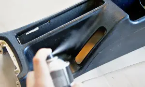 Ręka trzyma puszkę z farbą w sprayu, odświeżając czarne plastiki w aucie.