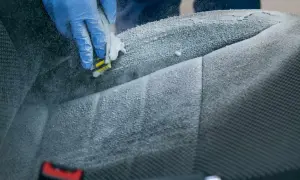 Rękawiczka w niebieskiej rękawicy szoruje fotel samochodowy, rozpoczynając proces prania foteli samochodowych.