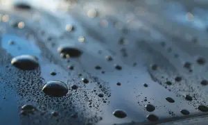 Krople wody na ciemnej powierzchni samochodu, świadczące o działaniu powłoki hydrofobowej.