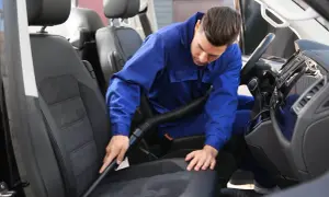 Mężczyzna w niebieskim kombinezonie odkurza siedzenie samochodu. Czy to alcantara? Co to za materiał?