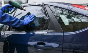 Ręce w niebieskich rękawiczkach przyciemniają szybę auta opalarką. Zastanawiasz się, przyciemnianie szyb ile procent wybrać?