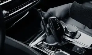 Rękawiczka z czarną rękawiczką delikatnie czyści szczoteczką błyszczące piano black w samochodzie, usuwając kurz.