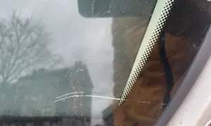 Głęboka rysa na szybie samochodowej, widoczna na tle rozmytego drzewa i budynku.