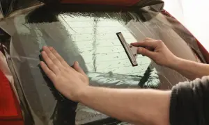 Nakładanie folii na tylną szybę samochodu. Ręce wygładzają folię, usuwając pęcherzyki powietrza, co jest kluczowe przy przyciemnianiu szyb od zewnątrz.