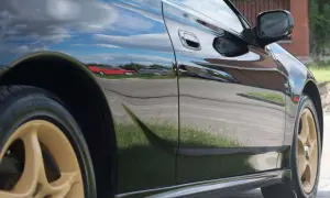 Błyszczące czarne uni auto z złotymi felgami odbija niebo i otoczenie.