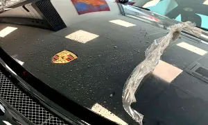 Czarna maska Porsche z logo, na której widać krople wody i fragment folii. Trwa klejenie folii na sucho.