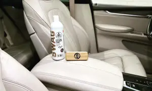 Zestaw do pielęgnacji jasnej skóry w samochodzie: butelka preparatu SWAG Leather Cleaner i drewniana szczotka. Idealne, by natłuścić skórę w samochodzie.