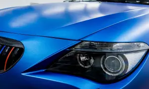 Matowy, **laguna blue** lakier na masce i błotniku sportowego auta. Widoczny fragment reflektora i grill z akcentami M.