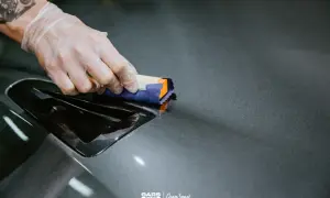Nakładanie ceramiki lakieru na ciemnoszary element samochodu. Ręka w rękawiczce aplikuje produkt.