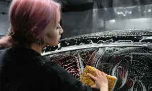Kobieta z różowymi włosami myje auto gąbką. Czy można myć samochód płynem do naczyń? Piana na karoserii sugeruje eksperyment.