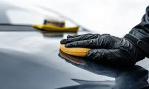 Rękawiczka w czarnej rękawicy rozprowadza wosk na ceramice, nadając jej połysk.