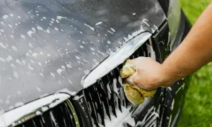 Ręczne mycie auta. Gąbka z pianą czyści grill ciemnego samochodu.