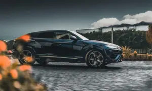 Luksusowy SUV w kolorze **midnight blue** pędzi po brukowanej drodze, otoczony bujną roślinnością i chmurami.