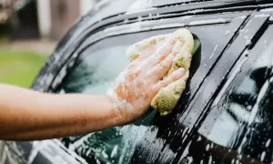 Ręka z gąbką myje okno samochodu, tworząc pianę. Dowiedz się, czym umyć auto, by lśniło czystością.