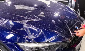 Niebieski **car color** z folią ochronną na masce. Widać krople wody i pęcherzyki powietrza pod folią.