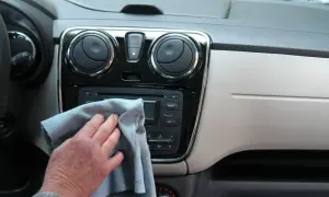 Ręka z szarą ściereczką czyści radio samochodowe i nawiewy. Dbałość o mycie detali w aucie.