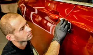 Detailer nakłada powłokę kwarcową czy ceramiczną na błyszczący, czerwony lakier samochodu, dbając o każdy detal.