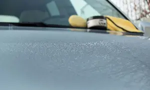 Krople wody na masce samochodu po woskowaniu. W tle widać gąbkę i słoik z woskiem.