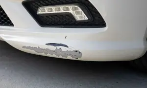Zderzak z widocznym, zdartym lakierem w kilku miejscach. Widać czarny podkład pod białym lakierem.