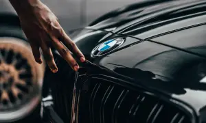 Dłoń dotyka błyszczącej maski czarnego BMW. Zastanawiasz się, ile schnie lakier bezbarwny po polerowaniu?