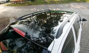 Błyszczące oklejenie dachu samochodu odbija drzewa i słońce. Eleganckie wykończenie dodaje autu stylu.