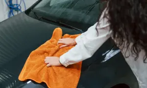 Kobieta z długimi włosami wykonuje mycie samochodu, używając pomarańczowego ręcznika do polerowania maski.