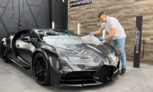 Mężczyzna aplikuje folię ochronną na maskę czarnego supersamochodu. Widać, ile folii na auto potrzeba do zabezpieczenia tego luksusowego pojazdu.
