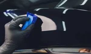 Ręka w czarnej rękawiczce nakłada niebieską glinkę na błyszczącą karoserię, wykonując serwis powłoki ceramicznej.