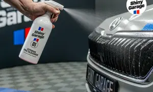 Ręka rozpyla pre-wash oprysk Citrus Pre Cleaner z butelki Shiny Garage na grill samochodu, usuwając brud.