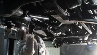 Mechanik w kombinezonie ochronnym wykonuje konserwację podwozia bez kanału, używając pistoletu do aplikacji środka.