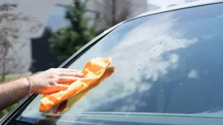 Ręka z pomarańczową ściereczką czyści szybę samochodu, pokazując, jak usunąć naklejkę z szyby.