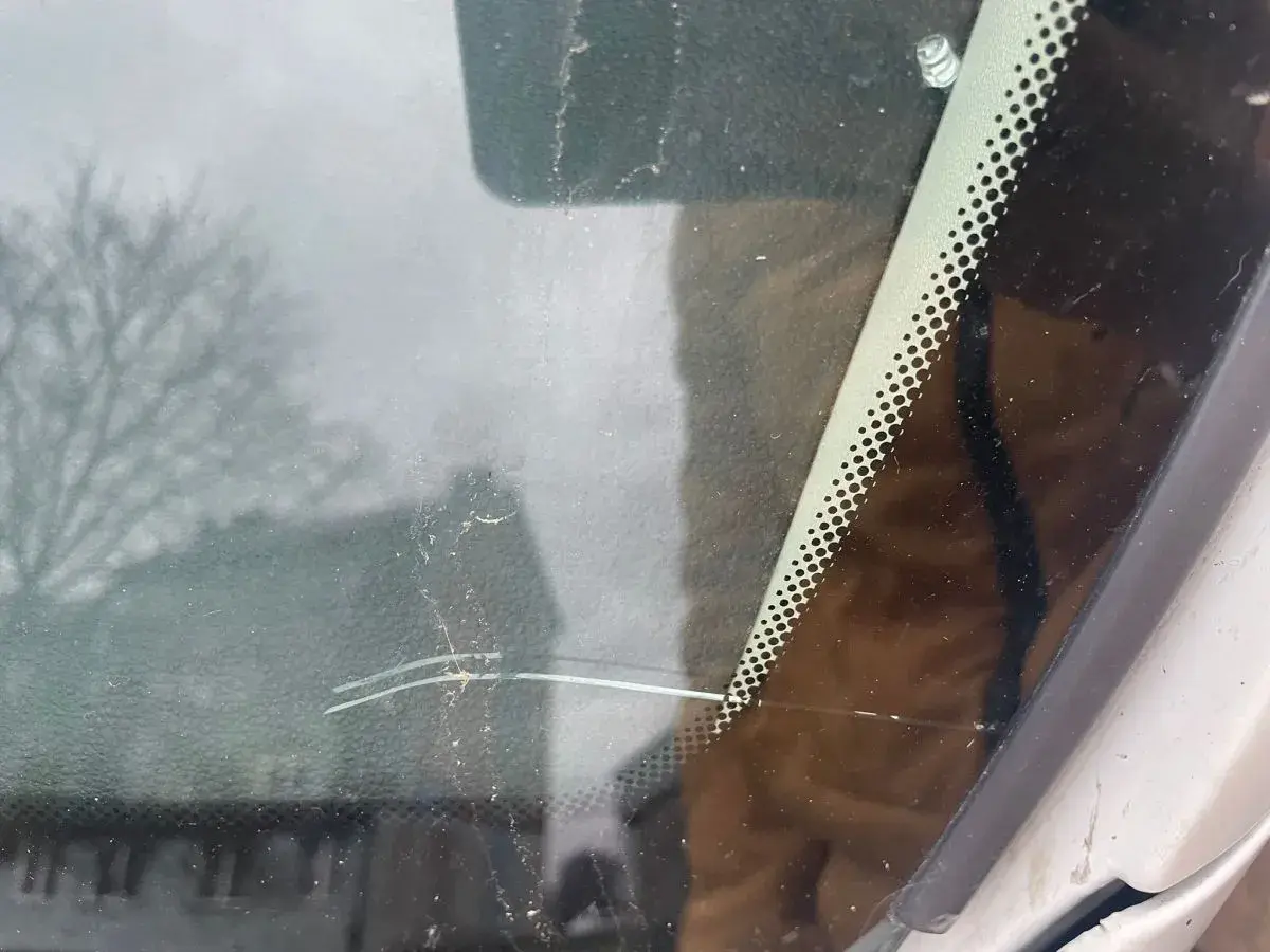 Głęboka rysa na szybie samochodowej, widoczna na tle rozmytego drzewa i budynku.