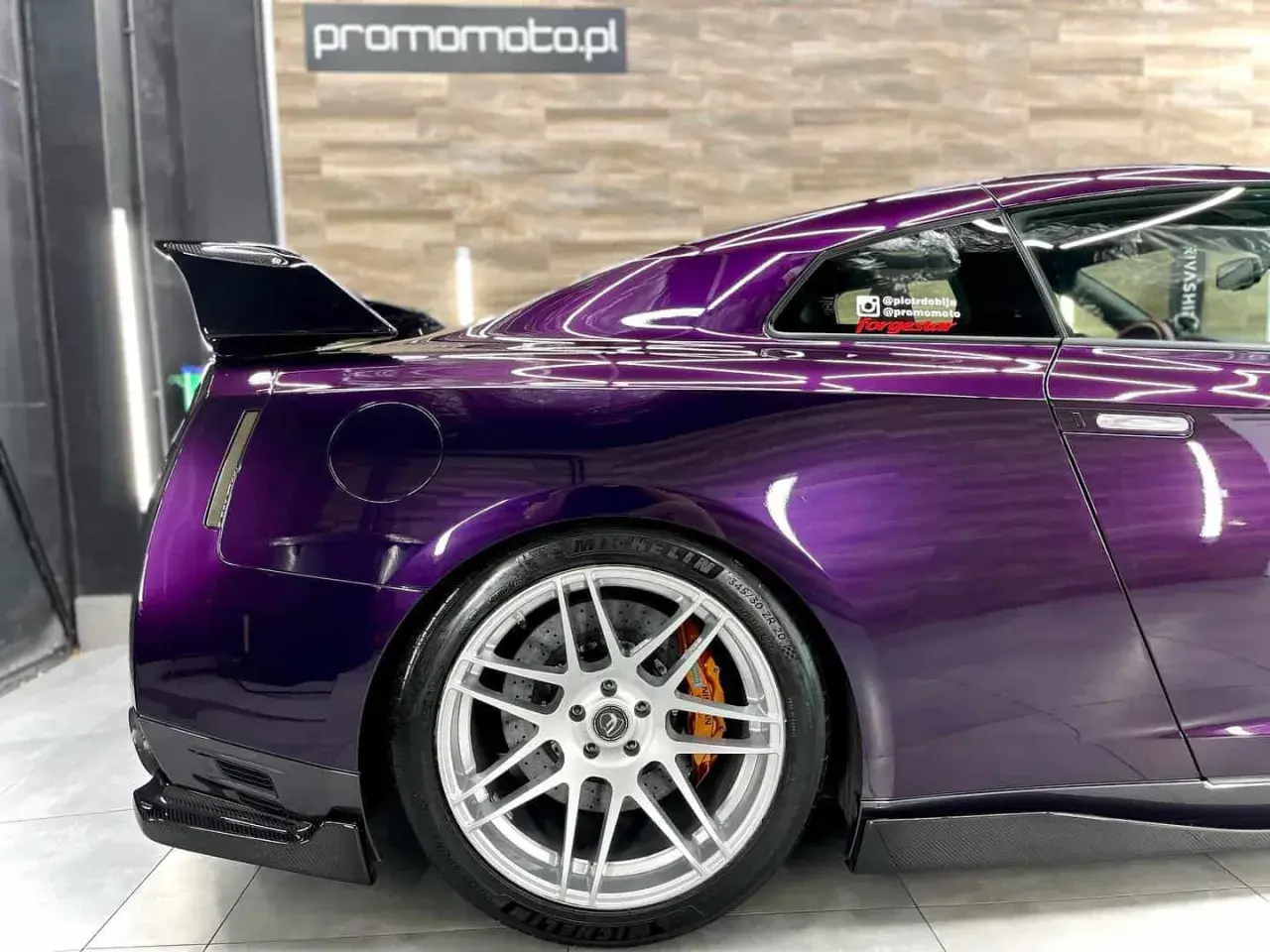 Sportowy Nissan GT-R w odcieniu **midnight purple**, z karbonowym spoilerem i felgami.