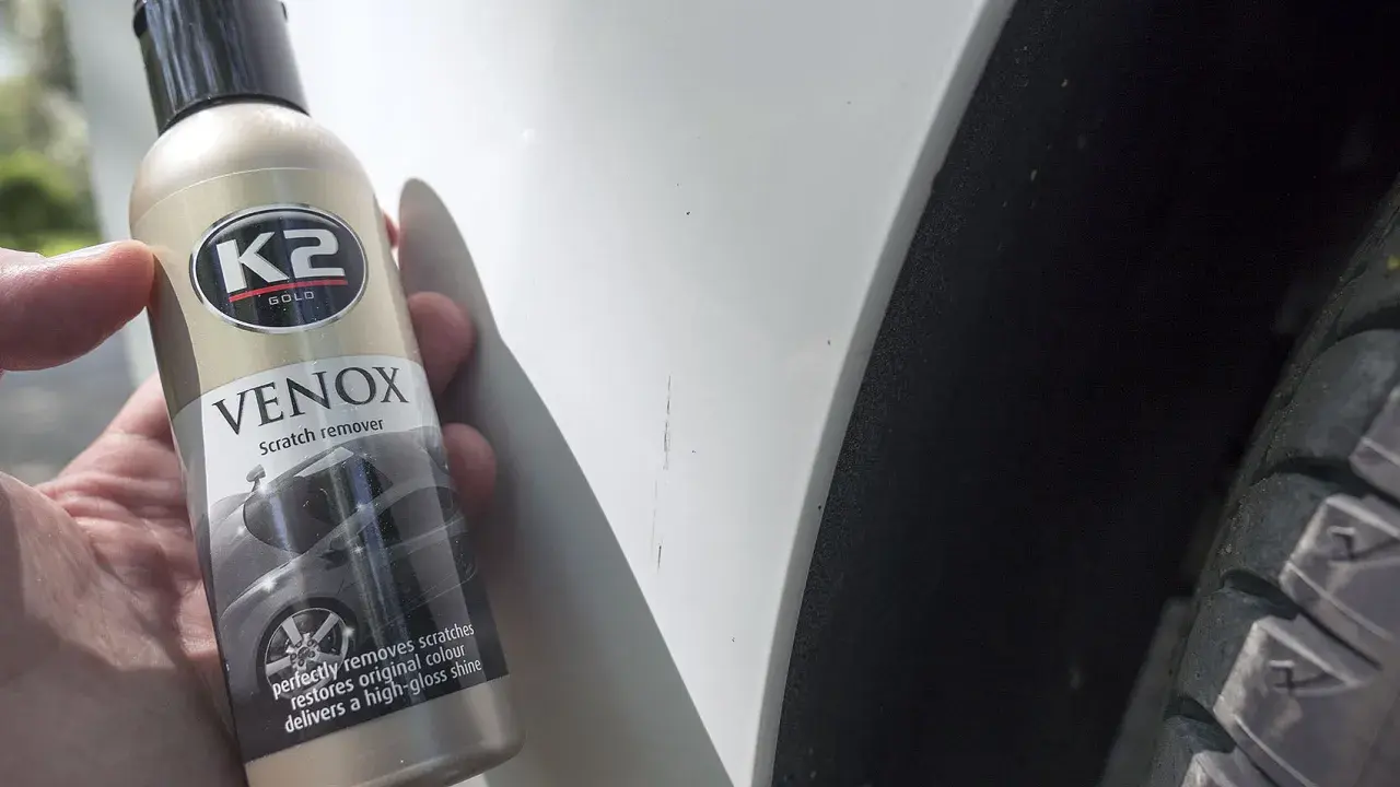 Jak usunąć głębokie rysy na lakierze? Butelka K2 VENOX Scratch remover obok białego lakieru z widocznymi zadrapaniami.