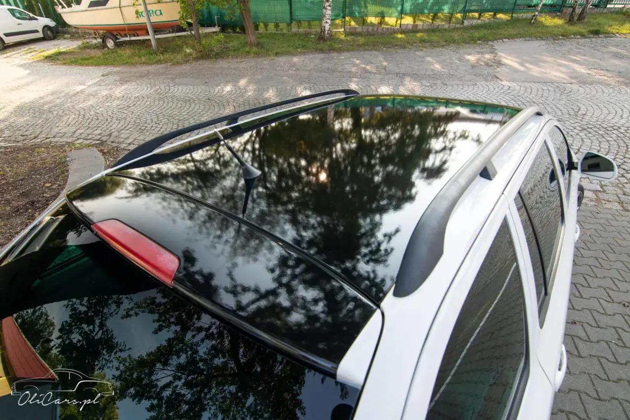 Błyszczące oklejenie dachu samochodu odbija drzewa i słońce. Eleganckie wykończenie dodaje autu stylu.
