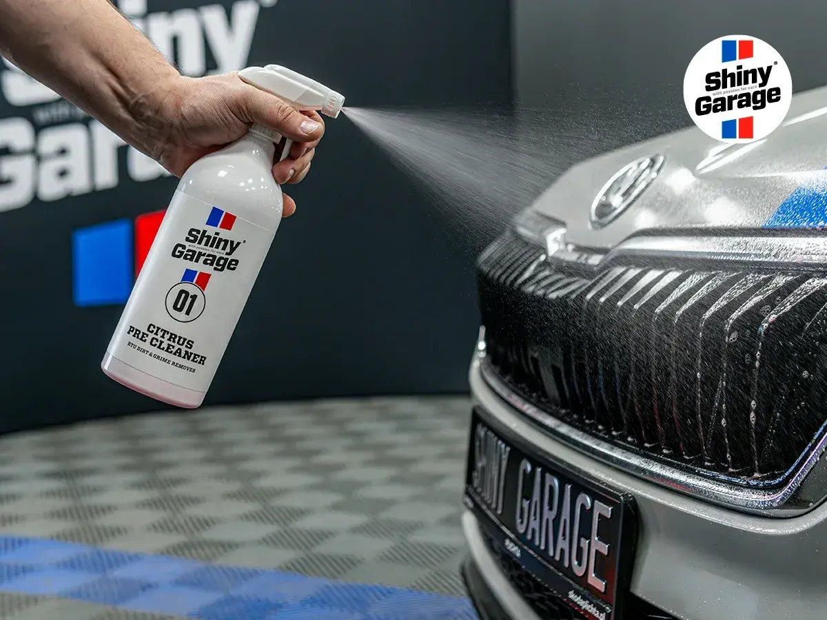 Ręka rozpyla pre-wash oprysk Citrus Pre Cleaner z butelki Shiny Garage na grill samochodu, usuwając brud.