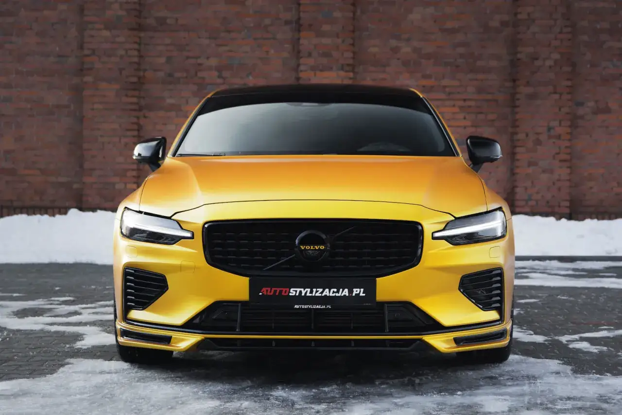Żółte Volvo S60 z czarnym grillem i detalami, oklejone folią Avery Dennison. Auto stoi na tle ceglanej ściany i ośnieżonego podjazdu.