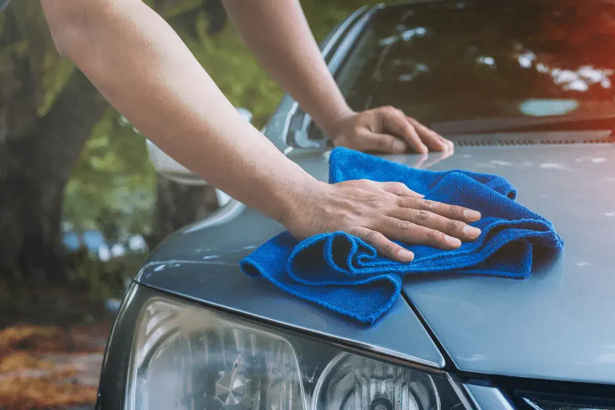 Ręce polerują maskę samochodu niebieską mikrofibrą, nadając jej połysk. To jak domowy wosk do samochodu, który sprawia, że auto lśni.