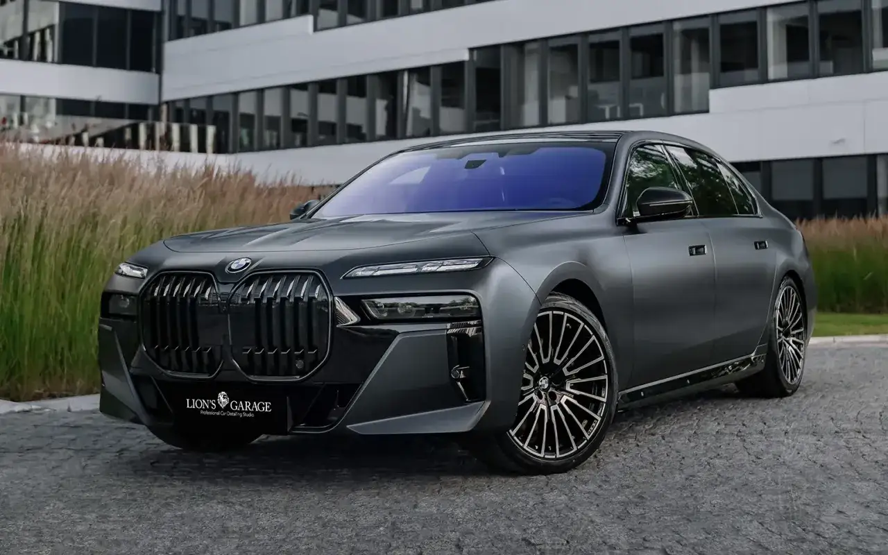 Matowy, grafitowy BMW Serii 7 z felgami Avery Dennison. Luksusowy sedan przed nowoczesnym budynkiem.