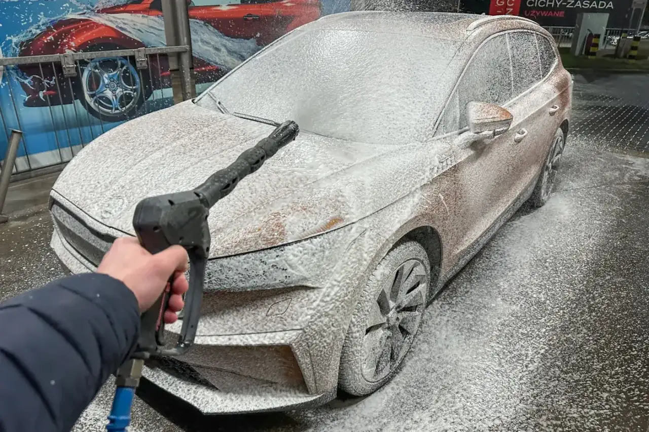 Myjnia bezdotykowa: triki na idealnie czyste auto. Pianka pokrywa karoserię, a ręka trzyma dyszę myjki.