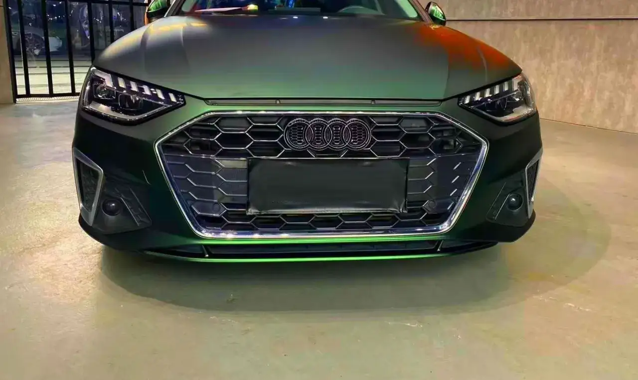 Przód lśniącego Audi w kolorze midnight green, z charakterystycznym grillem i ostrymi światłami.